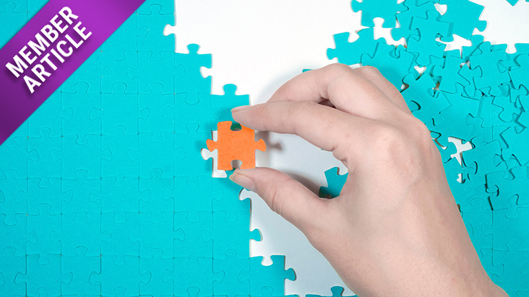 Stock picture of a hand putting an orange jigsaw piece in a half-completed turquoise puzzle